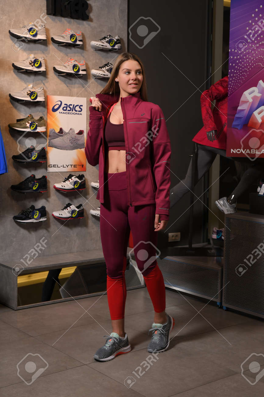 Skopje, Northern Macedonia - March 12, 2021: Asix store in Skopje, Northern Macedonia. Girl photo model wearing a set of dark red tracksuits and sneakers ASICS GEL, standing posing in a sports shop - 166164677 Skopje, Northern Macedonia - March 12, 2021: Asix store in Skopje, Northern Macedonia. Girl photo model wearing a set of dark red tracksuits and sneakers ASICS GEL, standing posing in a sports shop - 166164677
