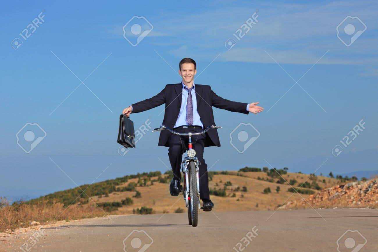 Carefree businessman holding a briefcase and riding a bicycle outdoors - 5652124 Carefree businessman holding a briefcase and riding a bicycle outdoors - 5652124