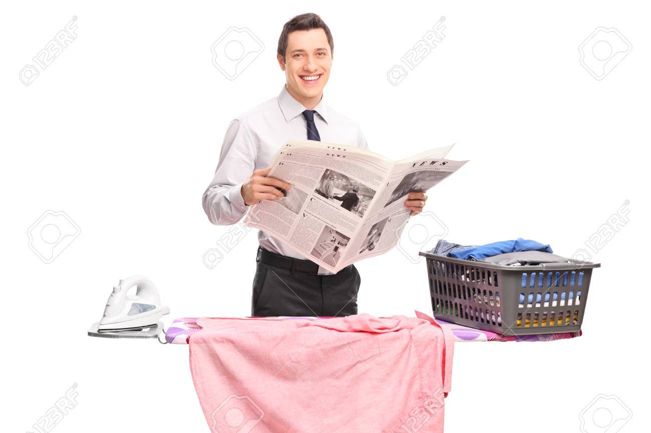 Cheerful Young Guy Holding A Newspaper And Posing Behind An Ironing Board Isolated On White Background Stock Photo Picture And Royalty Free Image Image