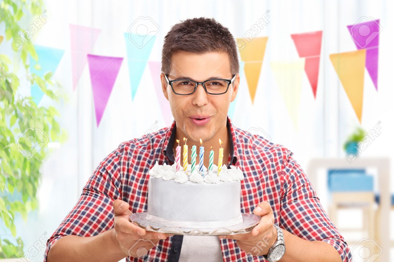 Joyful Jeune Homme Soufflant Les Bougies Sur Un Gateau D Anniversaire Et En Regardant La Camera A La Maison Banque D Images Et Photos Libres De Droits Image