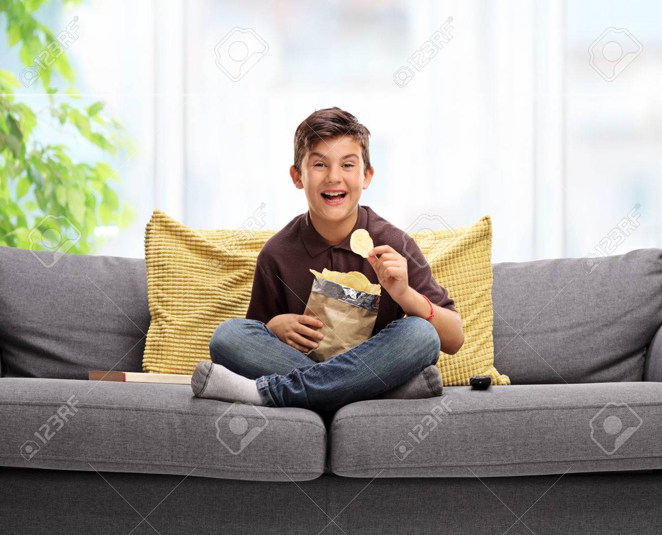 Joyful little boy sitting on a sofa and eating potato chips - 65941460 Joyful little boy sitting on a sofa and eating potato chips - 65941460