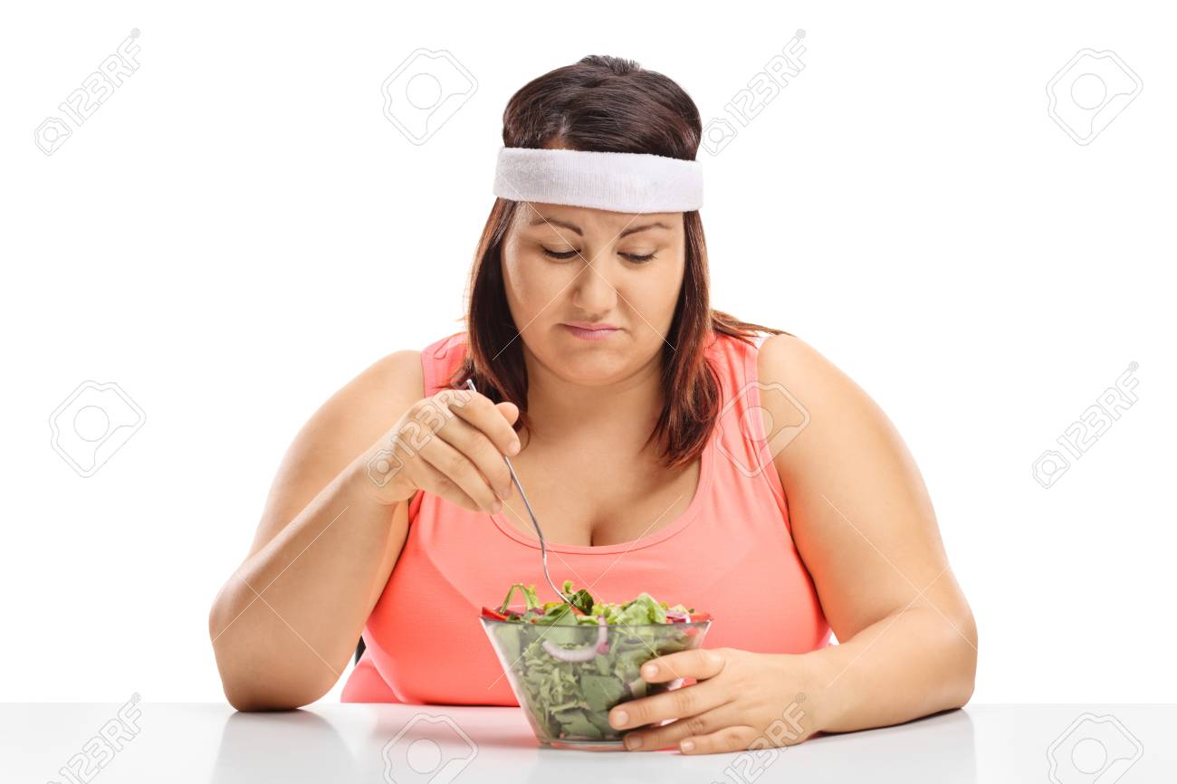 Sad overweight woman sitting at a table and looking at a bowl of salad isolated on white background - 89306213 Sad overweight woman sitting at a table and looking at a bowl of salad isolated on white background - 89306213