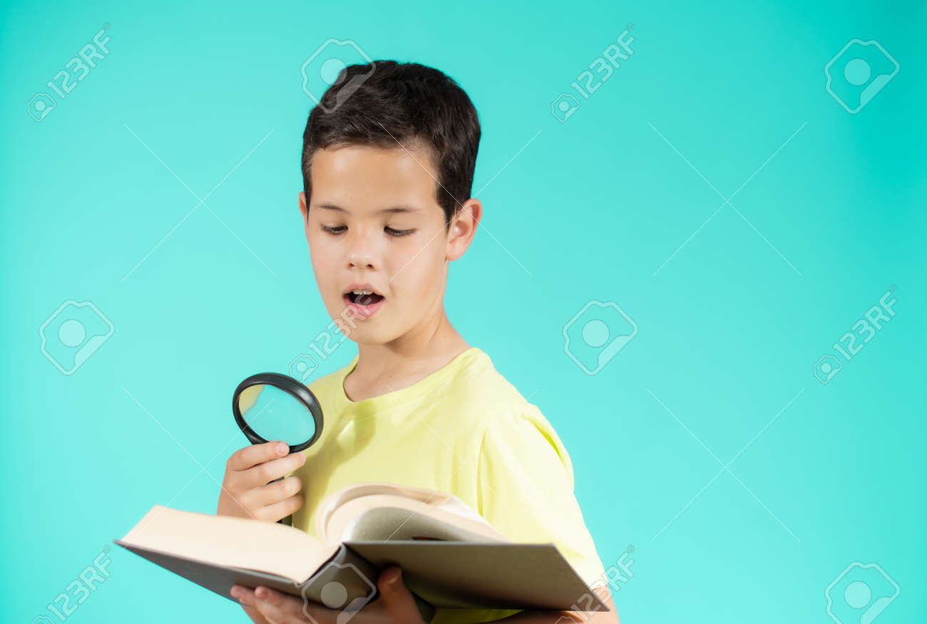 Young boy looking through a magnifying glass while reading an open book, isolated on green background - 166115483 Young boy looking through a magnifying glass while reading an open book, isolated on green background - 166115483