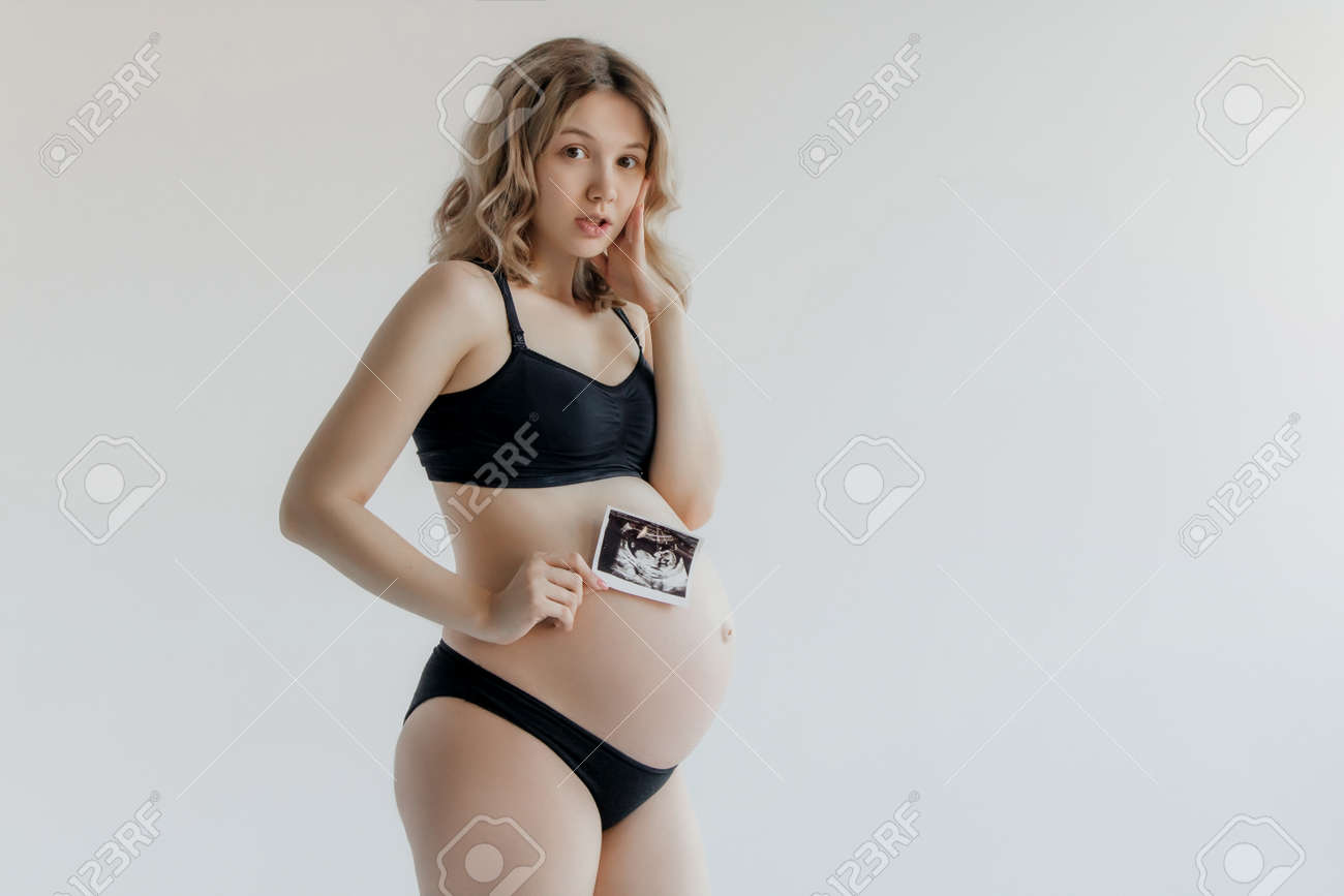 Examen Ecográfico Prenatal. Belleza Una Imagen De Sonograma Del Bebé Por Nacer Dentro De Su Gran Barriga. Feliz Futura Mamá Que Muestra La Imagen De Escaneo Del Feto Usi
