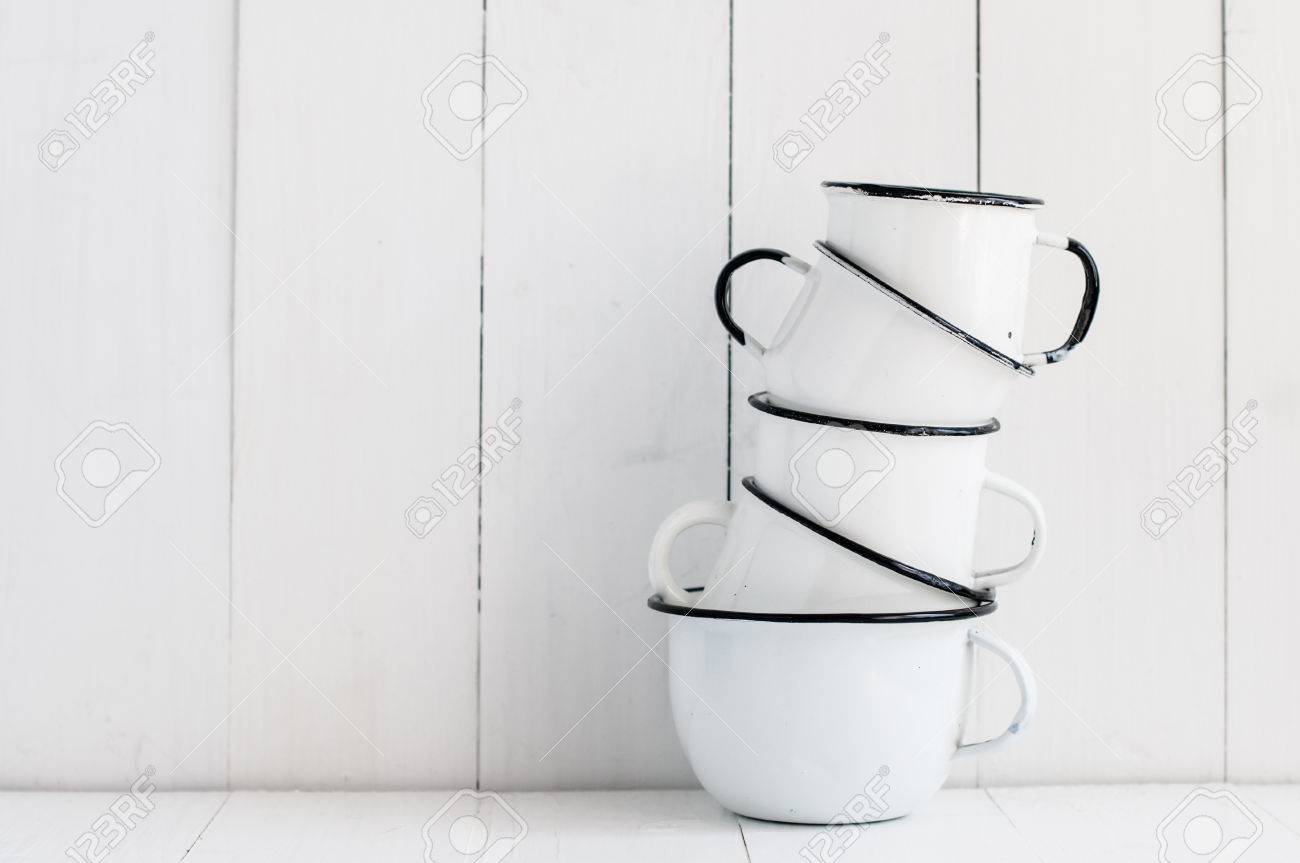 White Kitchen Utensils a stack of five white enameled mugs on painted wooden table White Kitchen Utensils a stack of five white enameled mugs on painted wooden table