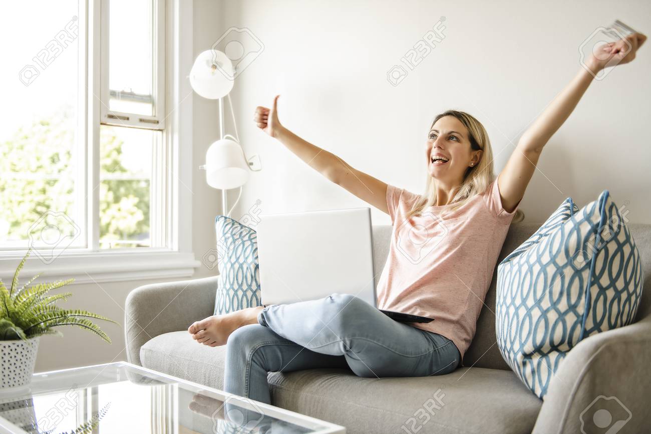 Happy Woman With A Credit Card And A Laptop On Sofa At Home Stock