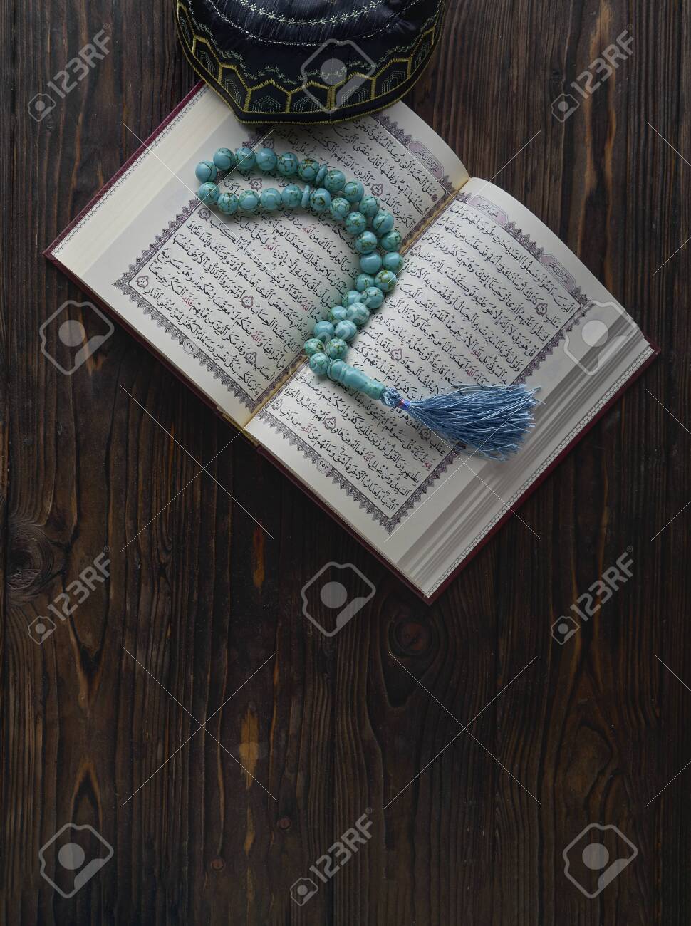 Open book Koran with rosary beads and muslim hat on wooden background. Islamic concept with copy space - 129083786 Open book Koran with rosary beads and muslim hat on wooden background. Islamic concept with copy space - 129083786