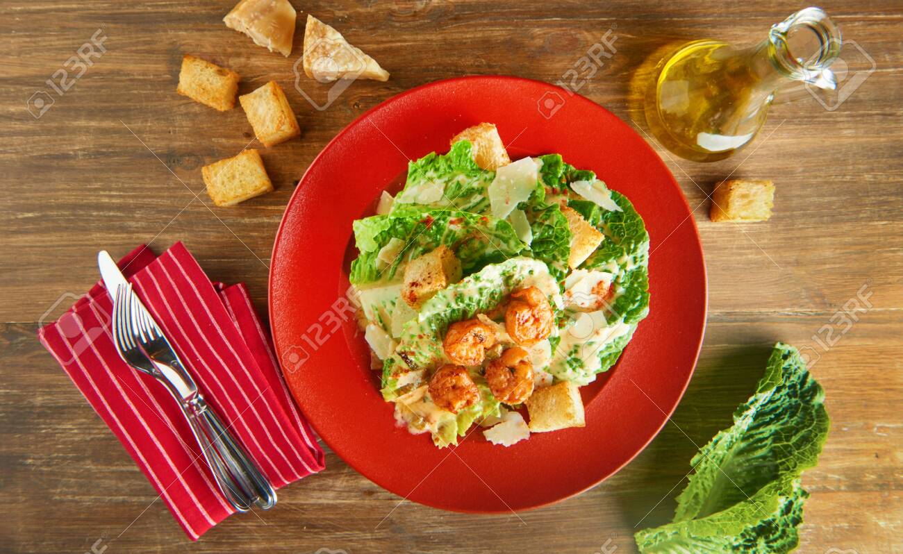 Fresh caesar salad on red plate with parmesan cheese and shrimps on wooden table. Top view - 131904945 Fresh caesar salad on red plate with parmesan cheese and shrimps on wooden table. Top view - 131904945