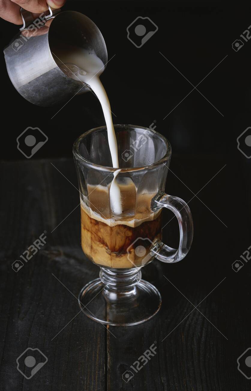 Hand pouring milk in cold brew coffee on black wooden table. - 131305989 Hand pouring milk in cold brew coffee on black wooden table. - 131305989