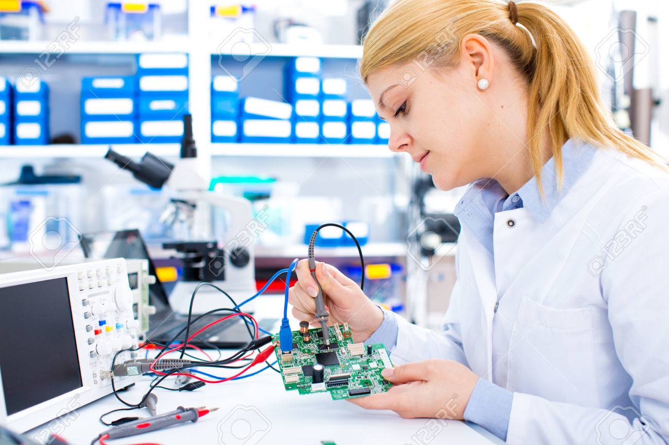 Engineer working with circuits. A woman engineer solders circuits sitting at a table. Microchip production factory. Technological process. Assembling the PCB board. Girl repairing electronic device on the circuit board. - 66767260 Engineer working with circuits. A woman engineer solders circuits sitting at a table. Microchip production factory. Technological process. Assembling the PCB board. Girl repairing electronic device on the circuit board. - 66767260