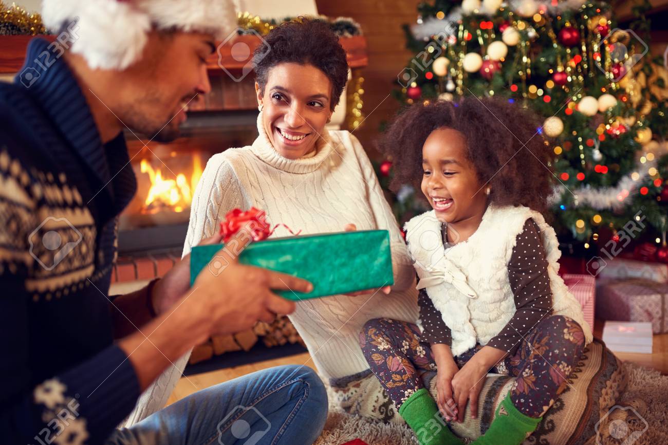 素敵な女の子の親からクリスマス プレゼントを受け取る暖炉の近くに幸せな家族の笑顔 の写真素材 画像素材 Image