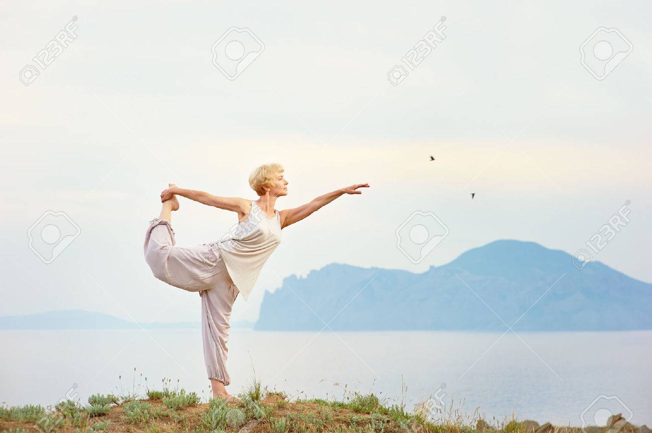 Senior woman doing yoga exercises with mountain on the background - 34185040 Senior woman doing yoga exercises with mountain on the background - 34185040