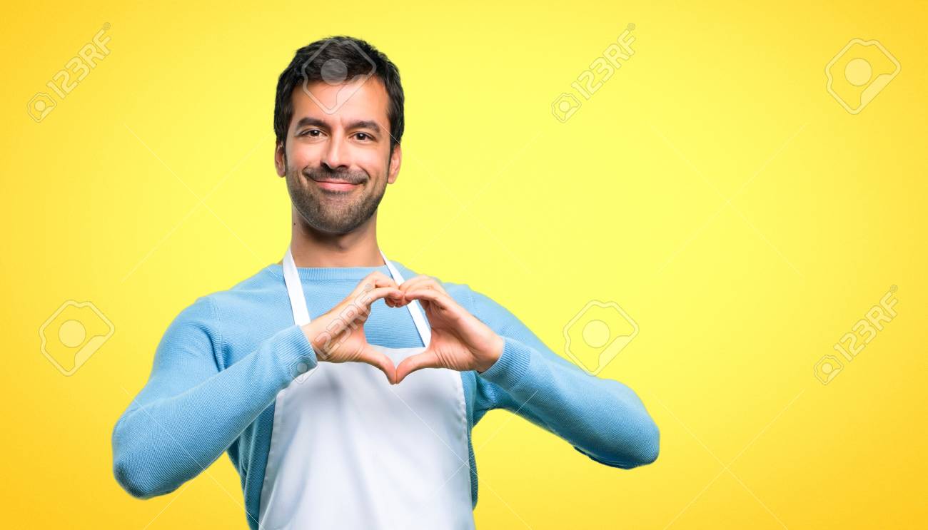 Man wearing an apron making heart symbol by hands. Being in love on yellow background - 113671151 Man wearing an apron making heart symbol by hands. Being in love on yellow background - 113671151