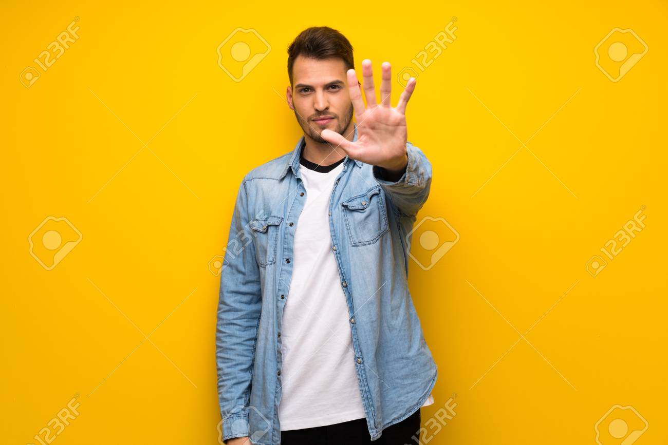 Handsome man over yellow wall making stop gesture denying a situation that thinks wrong - 119131978 Handsome man over yellow wall making stop gesture denying a situation that thinks wrong - 119131978