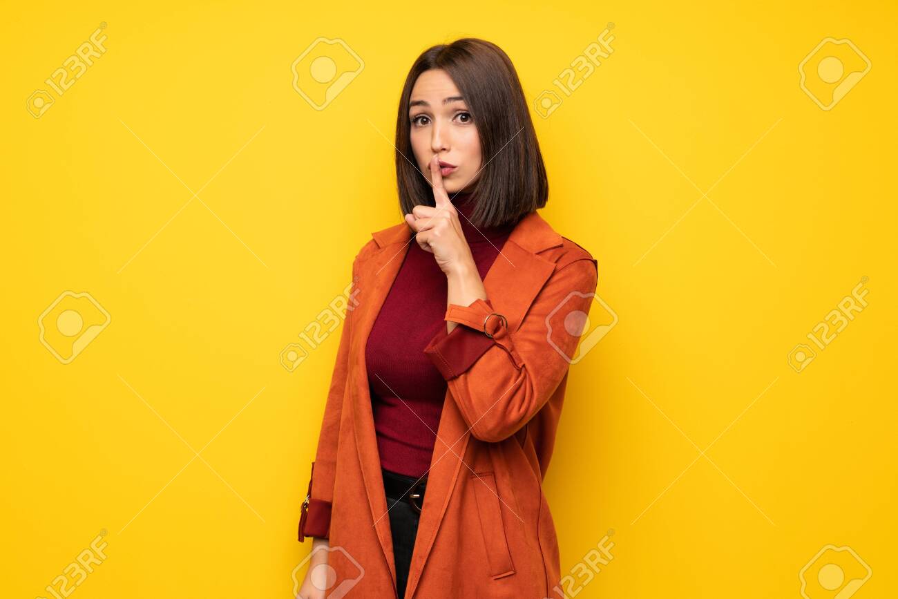 Young woman with coat showing a sign of silence gesture putting finger in mouth - 119423101 Young woman with coat showing a sign of silence gesture putting finger in mouth - 119423101