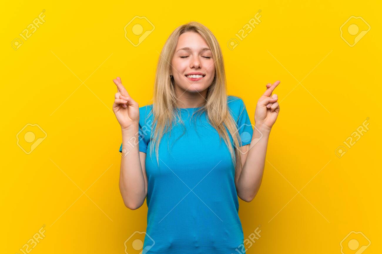 Young blonde woman over isolated yellow background with fingers crossing and wishing the best - 126981567 Young blonde woman over isolated yellow background with fingers crossing and wishing the best - 126981567