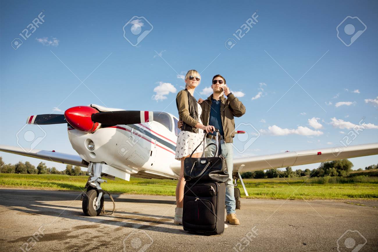 young couple standing by propeller airplane man using phone stock