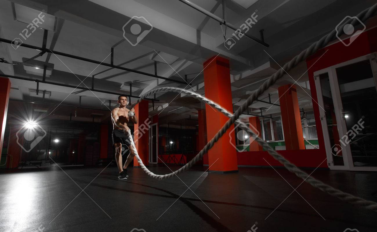Fitness man working out with battle ropes at gym. Battle ropes fitness man at gym workout exercise fitted body. Fitness man training with battle rope in fitness club. Training with battle rope - 66273078 Fitness man working out with battle ropes at gym. Battle ropes fitness man at gym workout exercise fitted body. Fitness man training with battle rope in fitness club. Training with battle rope - 66273078