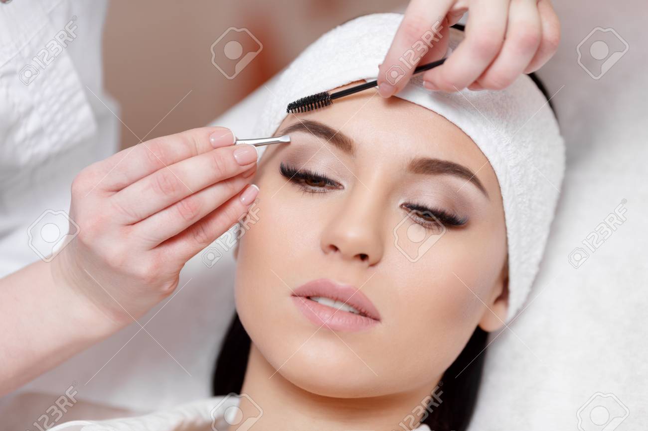 Permanent makeup. Beautiful young woman gets eyebrow correction procedure. Young woman tweezing her eyebrows in beauty saloon. Young woman plucking eyebrows with tweezers close up - 67853588 Permanent makeup. Beautiful young woman gets eyebrow correction procedure. Young woman tweezing her eyebrows in beauty saloon. Young woman plucking eyebrows with tweezers close up - 67853588