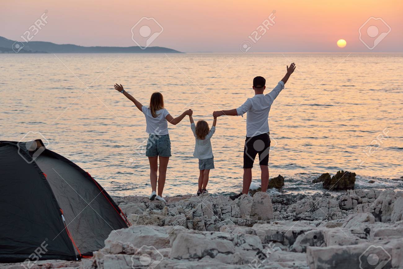 Back view of sweet young family, standing with open hands on rock beach and enjoying setting sun over sea. Mom, dad and little daughter holding hand and having best time together at summer vacation. - 106357560 Back view of sweet young family, standing with open hands on rock beach and enjoying setting sun over sea. Mom, dad and little daughter holding hand and having best time together at summer vacation. - 106357560