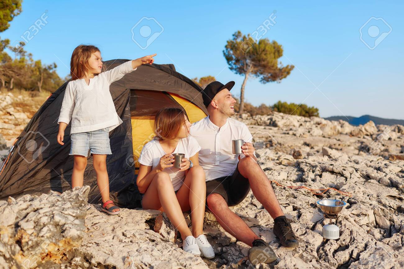 Family sitting near tent at rock beach admiring summer vacation. - 122905195 Family sitting near tent at rock beach admiring summer vacation. - 122905195