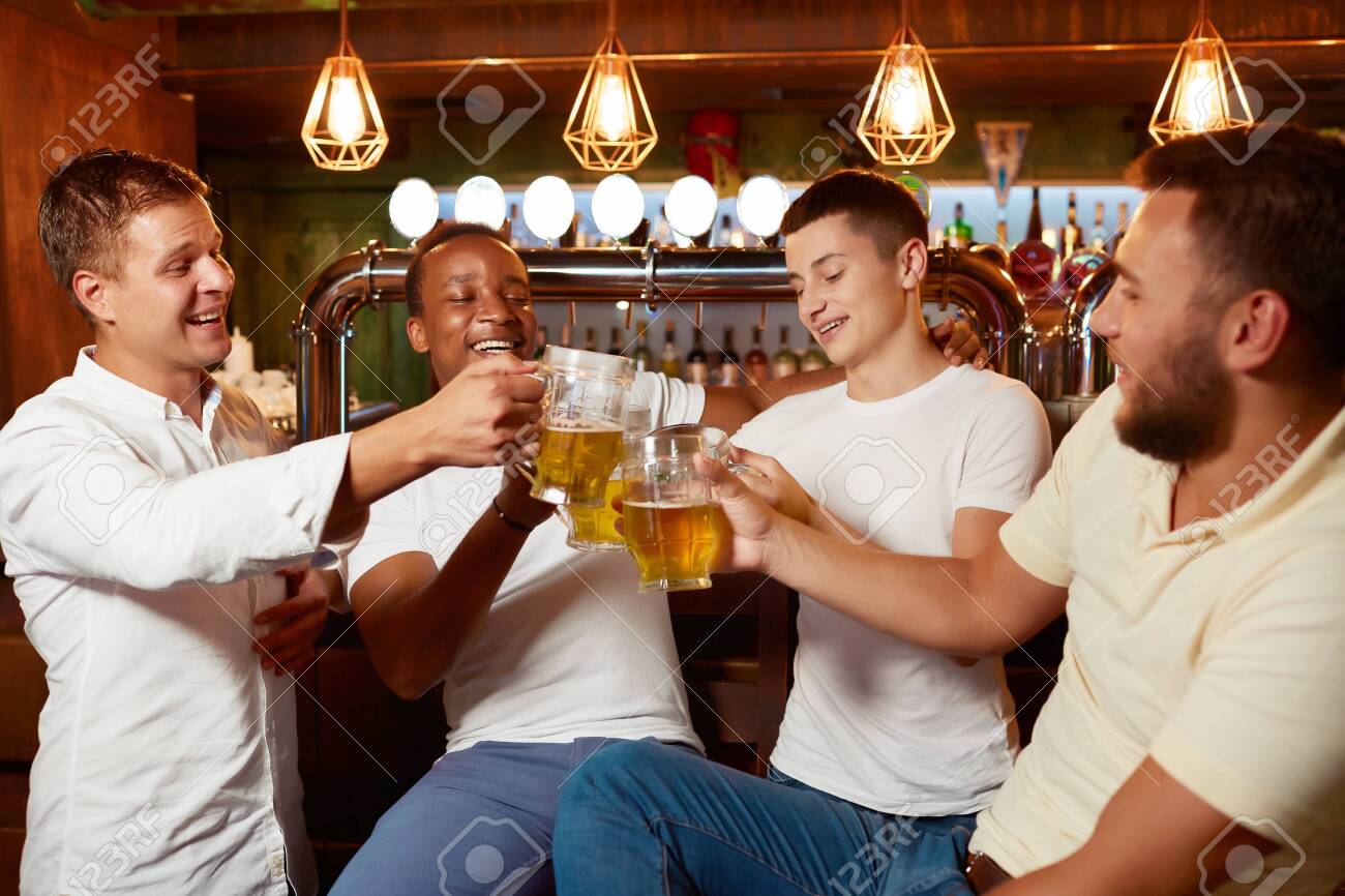 Four handsome men drinking beer together at pub clinking glasses. - 122913407 Four handsome men drinking beer together at pub clinking glasses. - 122913407