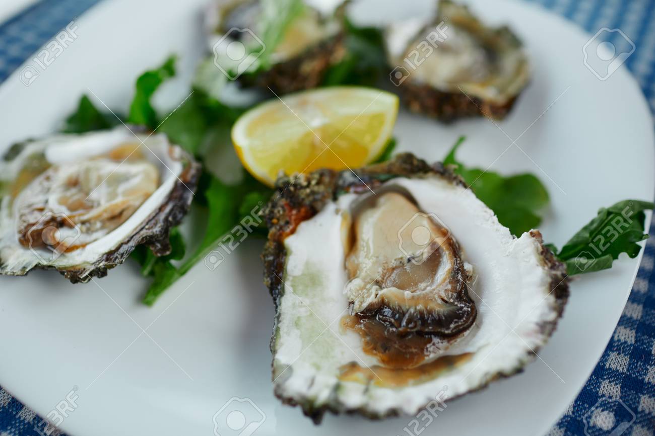 Fresh oysters on a white plate with green salad and lemon on a blue tablecloth - 126906733 Fresh oysters on a white plate with green salad and lemon on a blue tablecloth - 126906733