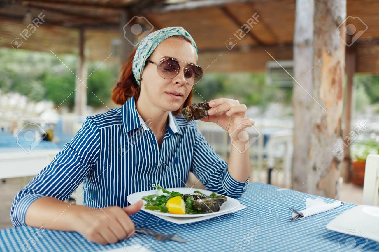 Young woman eating oyster in an outdoor restaurant - 122913415 Young woman eating oyster in an outdoor restaurant - 122913415
