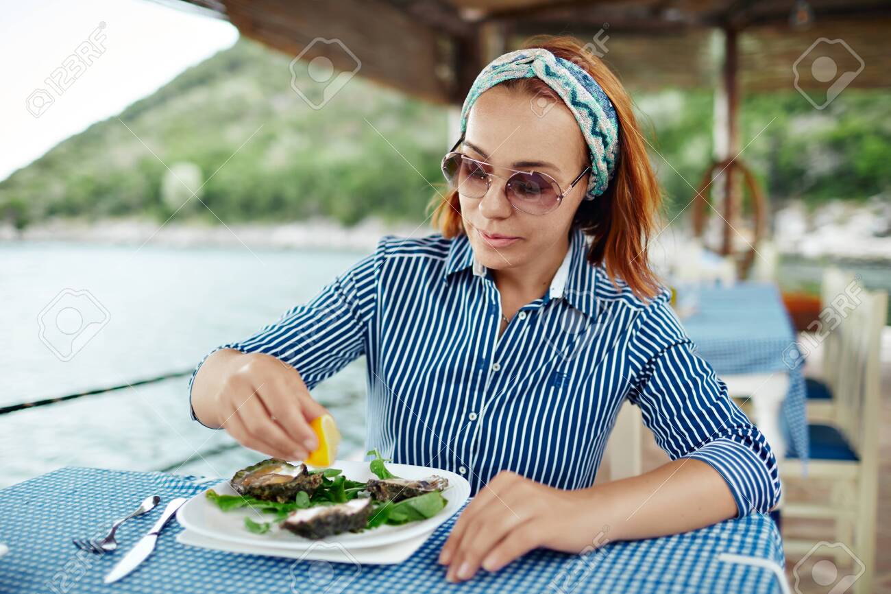 Woman eating a delicacy oyster, close-up outdoor restaurant - 122913416 Woman eating a delicacy oyster, close-up outdoor restaurant - 122913416