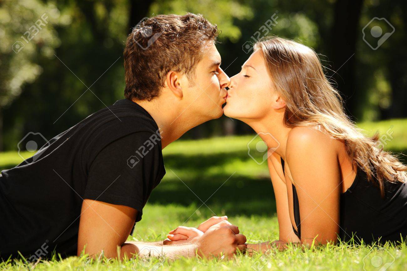 a young cute couple lying on the grass in the park and kissing stock