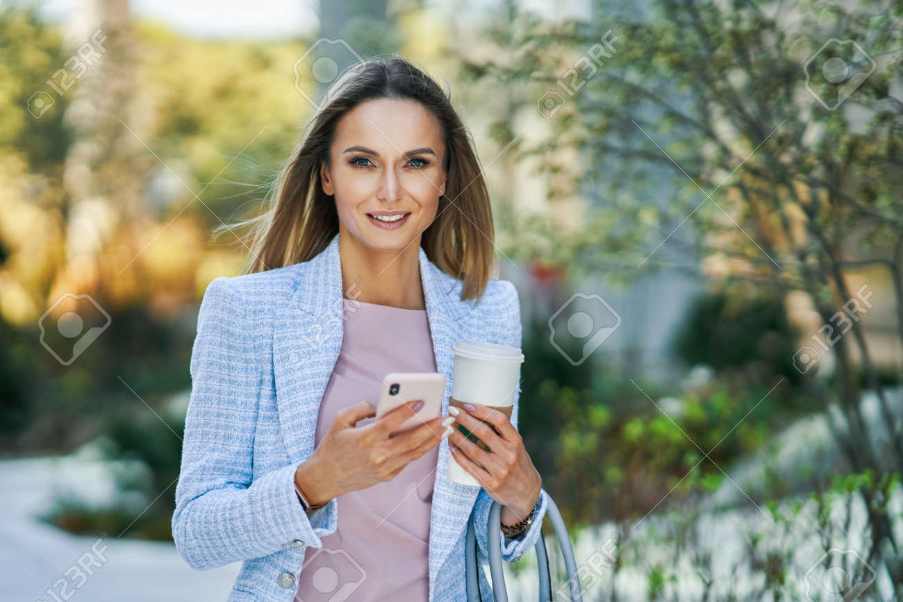 Adult attractive Business woman with smartphone and coffee walking in the city - 169882315 Adult attractive Business woman with smartphone and coffee walking in the city - 169882315