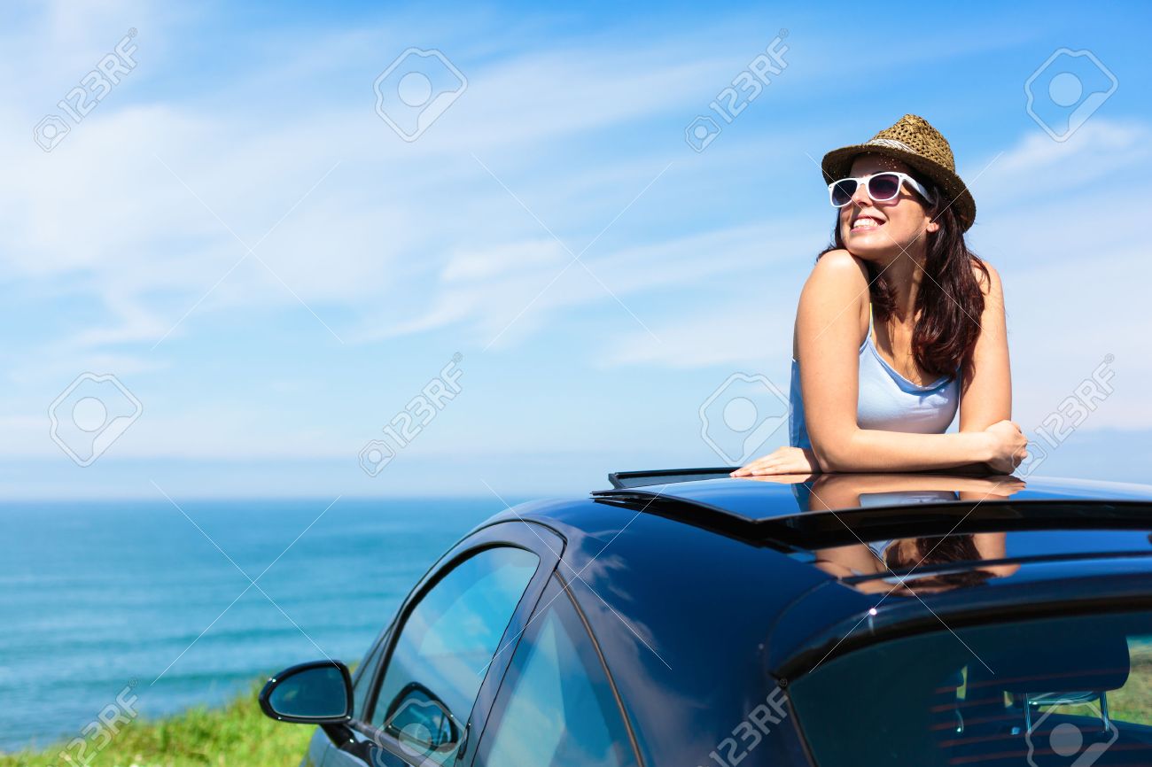 Relaxed happy woman on summer travel vacation to the coast leaning out car sunroof with the sea on background - 27578002 Relaxed happy woman on summer travel vacation to the coast leaning out car sunroof with the sea on background - 27578002
