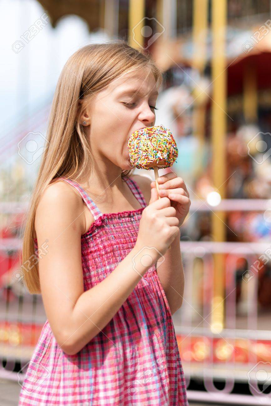 遊園地でフェアでリンゴ飴を食べるかわいい女の子 の写真素材 画像素材 Image