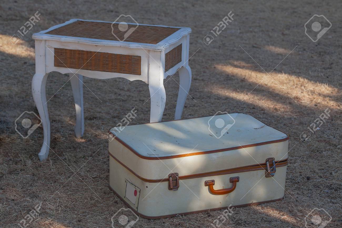 Old white suitcase on the grass and a wicker table close-up. - 89438026 Old white suitcase on the grass and a wicker table close-up. - 89438026