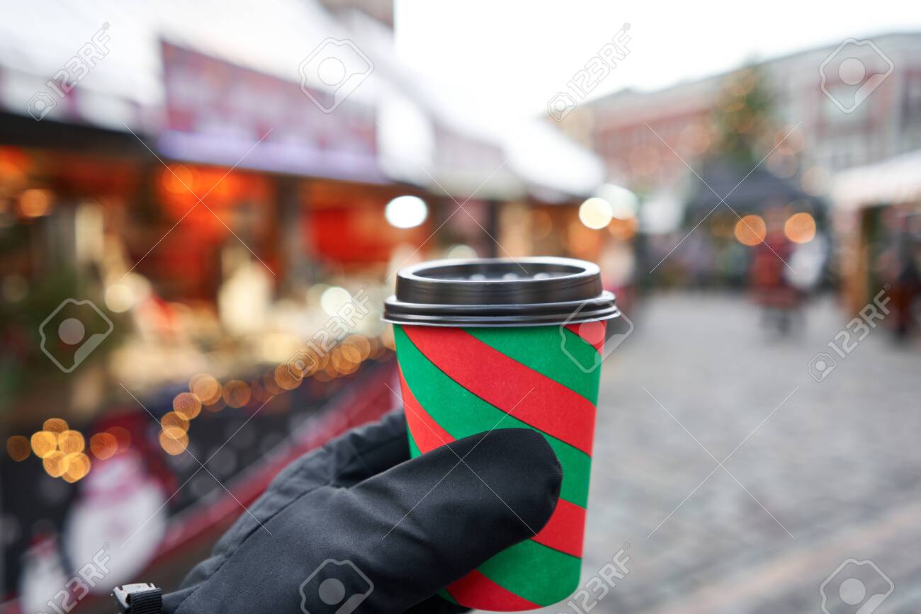 Hand holding a cup of mulled wine with blurred background of winter wonderland, a Christmas Market in European small city. - 135518611 Hand holding a cup of mulled wine with blurred background of winter wonderland, a Christmas Market in European small city. - 135518611
