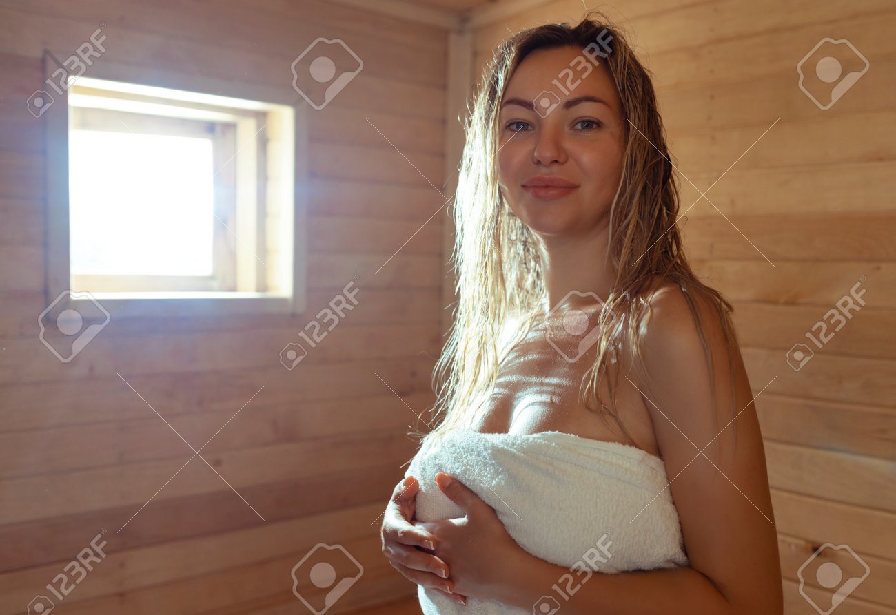 A Young Woman Relaxes And Sweats In A Hot Sauna Wrapped In A Towel. Girl In  The Sauna. Finnish Sauna Interior, Classic Wooden Sauna With Hot Steam.  Russian Bath. Фотография, картинки, изображения