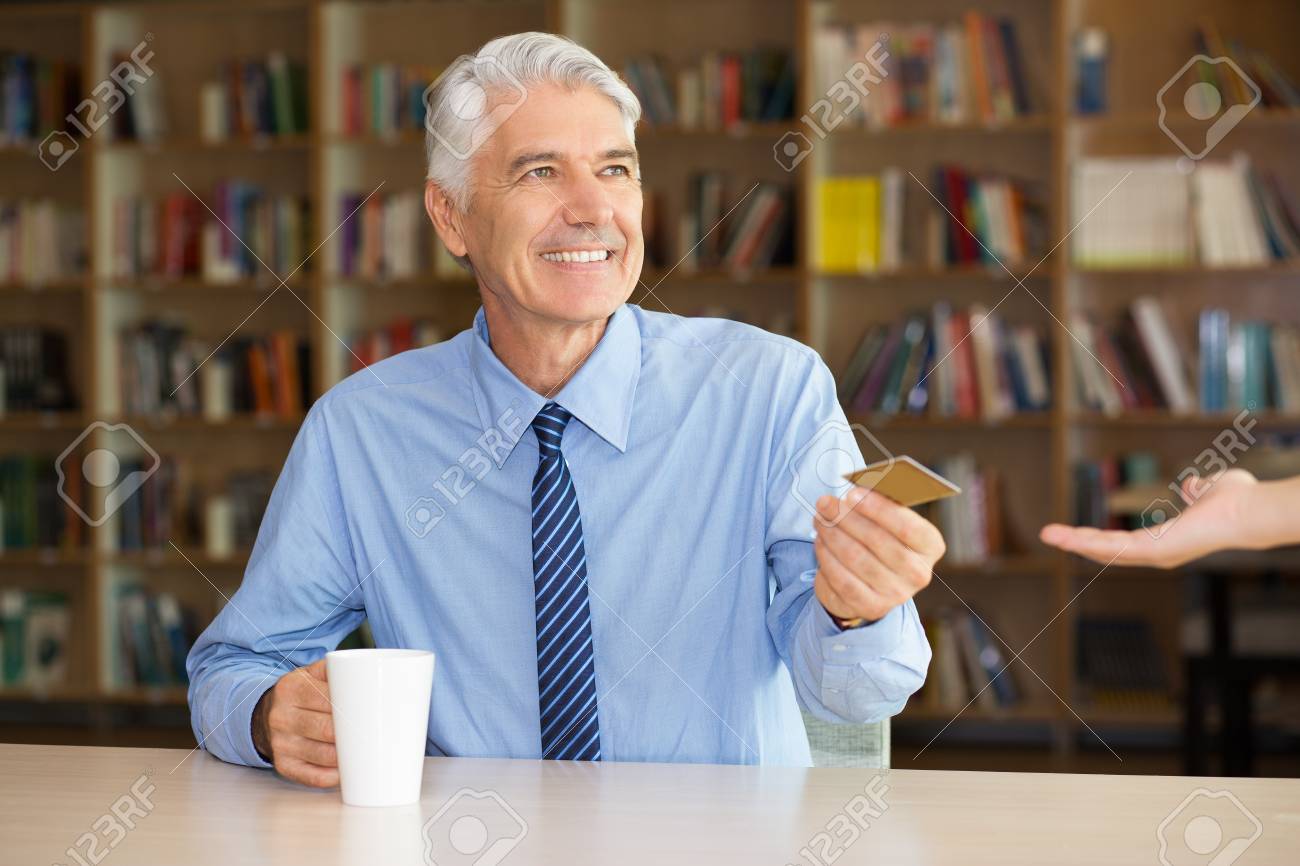 Happy senior businessman giving credit card to waitress to pay for coffee. Positive manager drinking coffee at table in library. Banking or convenient service concept - 67105014 Happy senior businessman giving credit card to waitress to pay for coffee. Positive manager drinking coffee at table in library. Banking or convenient service concept - 67105014
