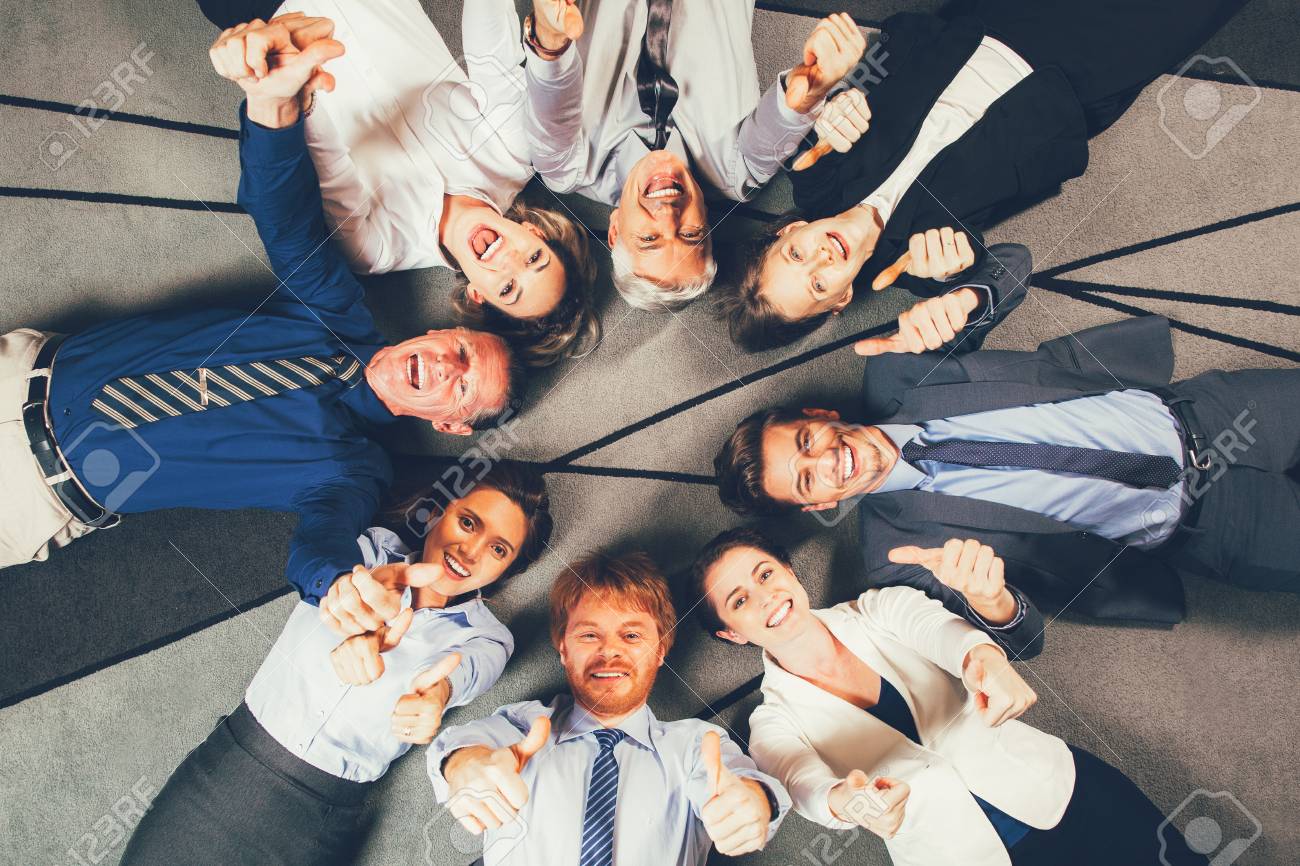 Business People Lying On Floor Showing Thumbs Up Stock Photo