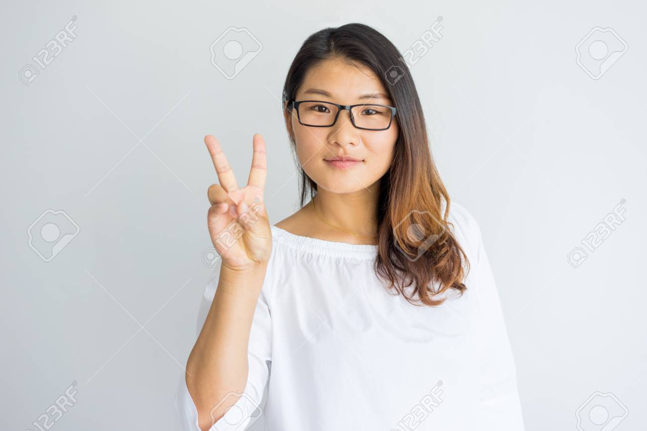 Content Attractive Chinese Woman In Eyeglasses Showing Greeting Gesture And Looking At Camera Positive Friendly Girl In White Blouse Showing Peace Sign Lifestyle Concept Stock Photo Picture And Royalty Free Image Image