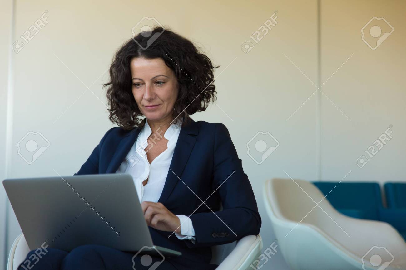 Satisfied businesswoman working on computer in office lounge and getting good news. Business woman sitting in armchair, using laptop, looking at screen and smiling. Wi-Fi concept - 130048861 Satisfied businesswoman working on computer in office lounge and getting good news. Business woman sitting in armchair, using laptop, looking at screen and smiling. Wi-Fi concept - 130048861