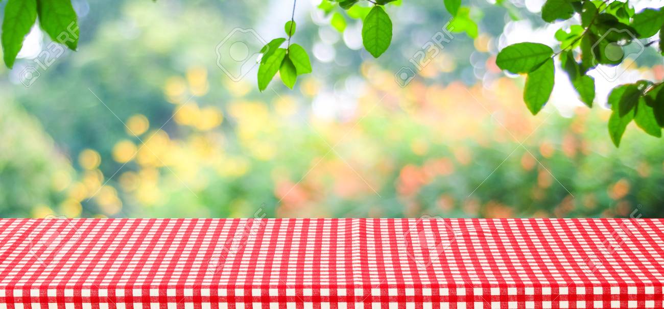 empty table with red tablecloth over blur green tree and bokeh