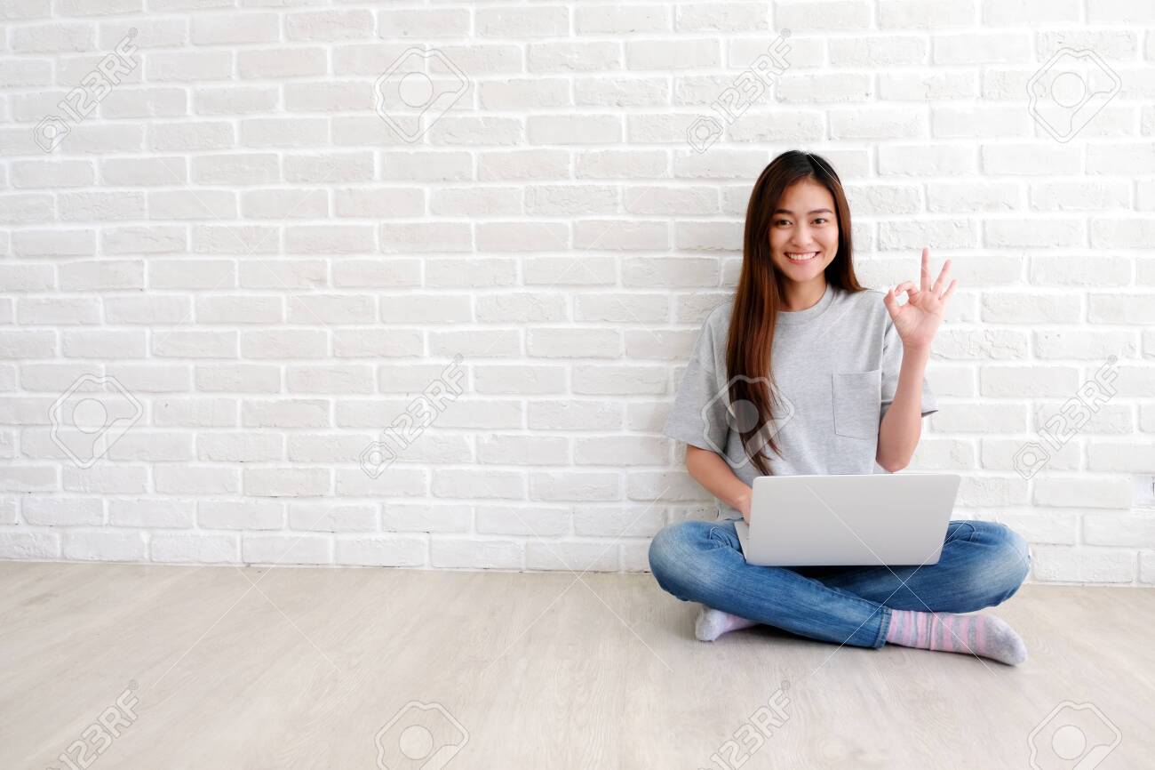 Young asian woman showing ok hand sign and smiling while working with laptop computer in white room with copy spce, people with positive gesture - 123741315 Young asian woman showing ok hand sign and smiling while working with laptop computer in white room with copy spce, people with positive gesture - 123741315
