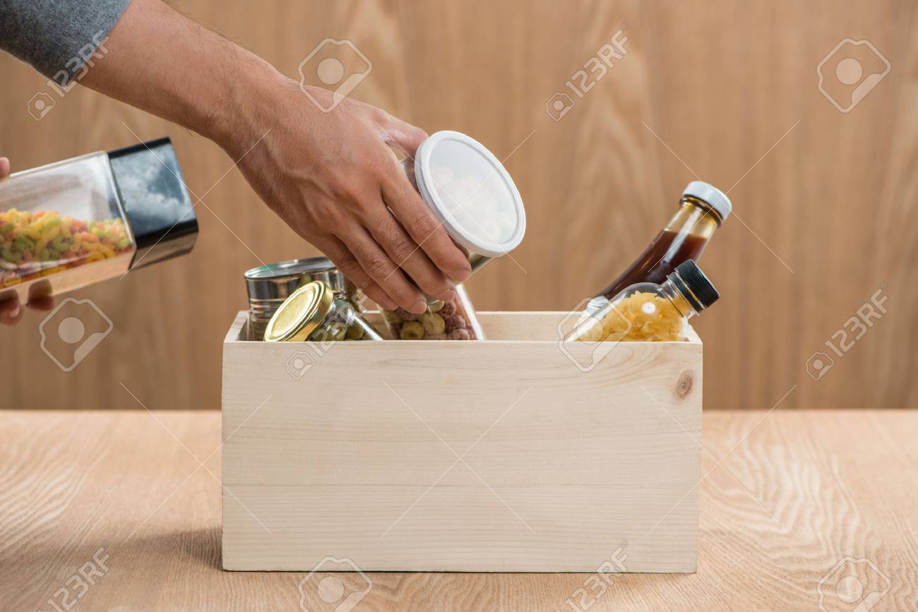 Volunteer with donation box with food stuffs on wooden background - 84984477 Volunteer with donation box with food stuffs on wooden background - 84984477