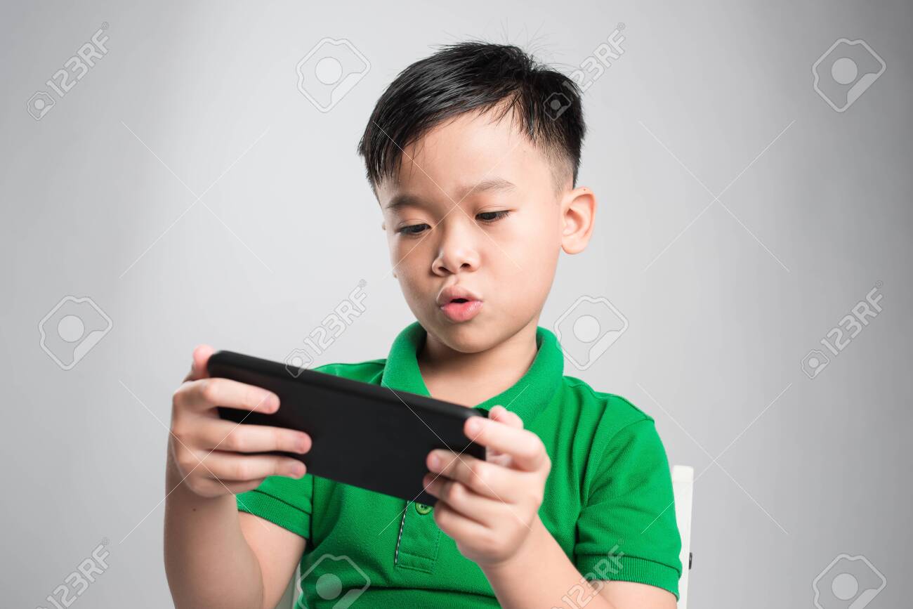 Portrait of an amused cute little kid playing games on smartphone isolated over gray background - 121037571 Portrait of an amused cute little kid playing games on smartphone isolated over gray background - 121037571