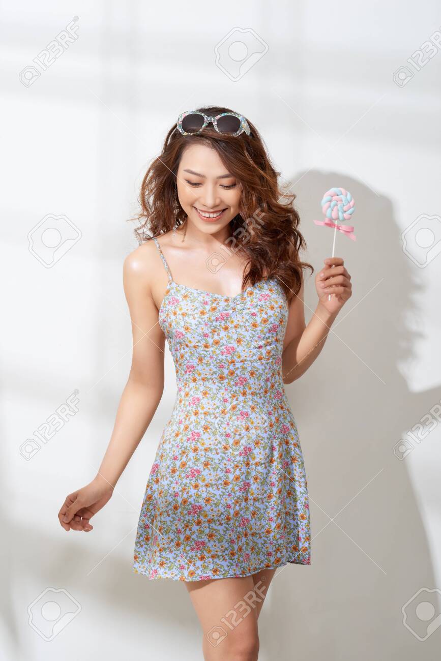 Attractive asian woman in flower dress with lollipop in hand - 124787470 Attractive asian woman in flower dress with lollipop in hand - 124787470
