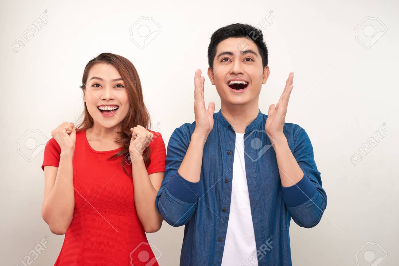 Young asian couple in love over isolated background celebrating surprised and amazed for success with arms raised and open eyes - 126710354 Young asian couple in love over isolated background celebrating surprised and amazed for success with arms raised and open eyes - 126710354