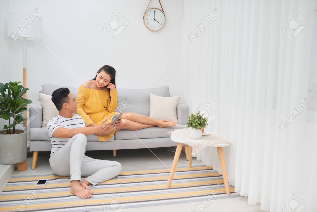 Young asian couple sitting on couch at home, using a tablet PC for Internet and social media. - 133121238 Young asian couple sitting on couch at home, using a tablet PC for Internet and social media. - 133121238