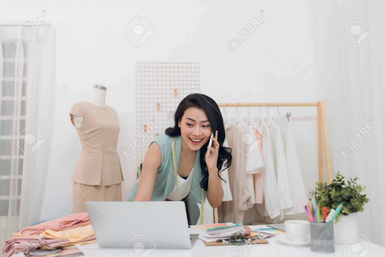 Beautiful seamstress using laptop and phoning while working at her workshop.Dressmaker using laptop - 133760733 Beautiful seamstress using laptop and phoning while working at her workshop.Dressmaker using laptop - 133760733