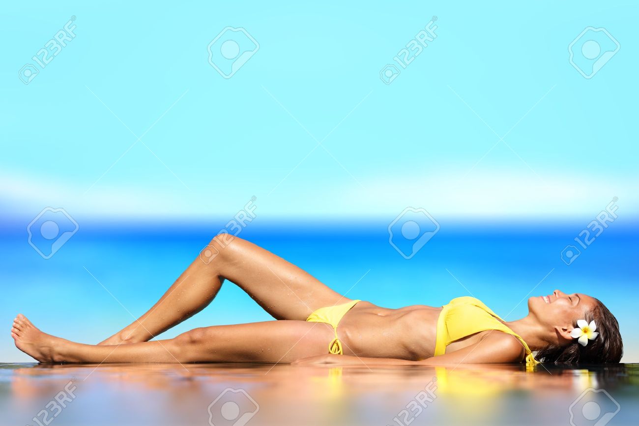 女性に彼女の背中に横になっている濡れている彼女のビキニで日光浴海辺で海の前の砂 の写真素材 画像素材 Image