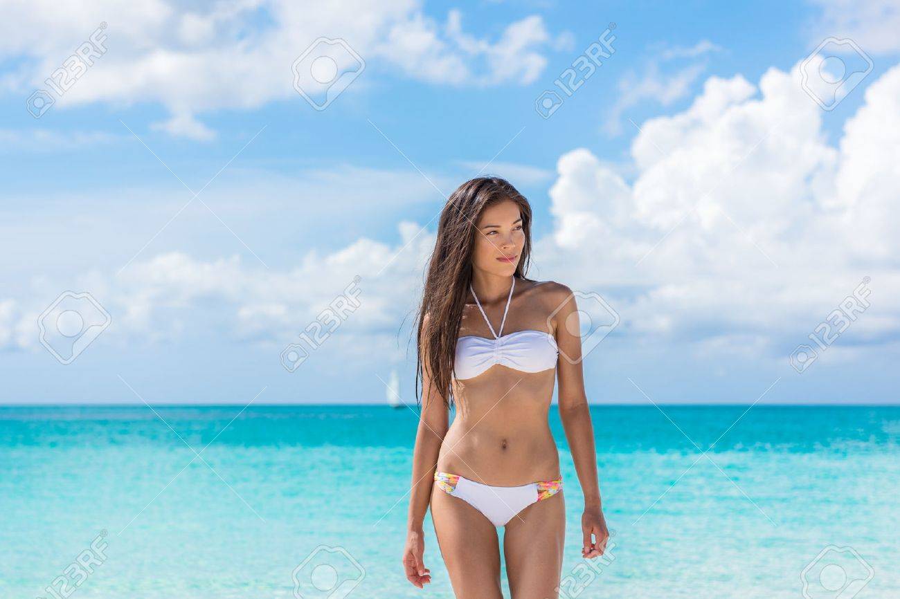 アジアのセクシーなビキニ女性が白いファッション水着を着てターコイズ ブルーの海の水から歩いてビーチにリラックス 肌や髪のケア女性モデル減量のためスリムなボディ の写真素材 画像素材 Image